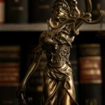 Close-up of a golden Lady Justice statue with scales in a law library setting.