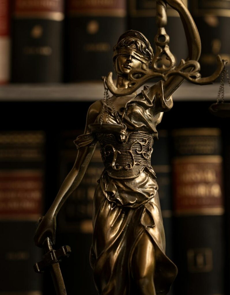 Close-up of a golden Lady Justice statue with scales in a law library setting.