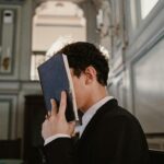 A young man in a suit prays with a book in a sunlit synagogue, capturing a moment of faith.