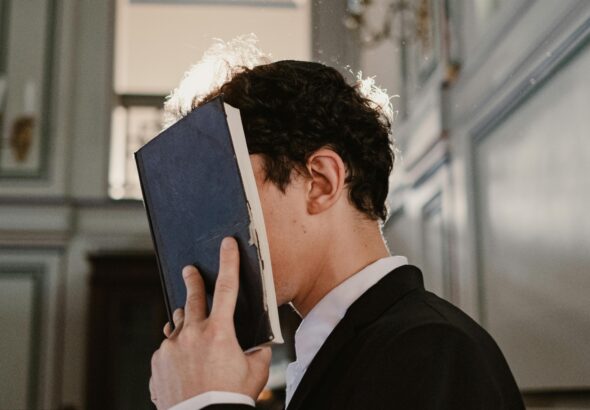 A young man in a suit prays with a book in a sunlit synagogue, capturing a moment of faith.