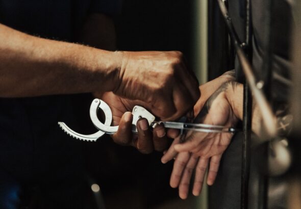 Close-up view of a person being handcuffed in a jail setting, focusing on hands and handcuffs.