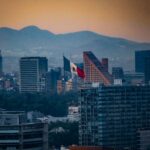 Stunning cityscape of Mexico City with the Mexican flag and mountains at sunset.