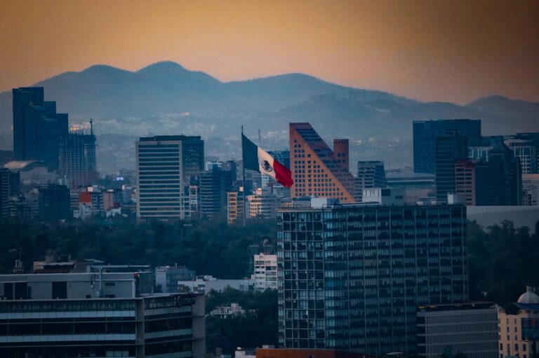 Stunning cityscape of Mexico City with the Mexican flag and mountains at sunset.