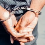 Close-up of an adult male's hands in handcuffs, symbolizing law enforcement and justice.